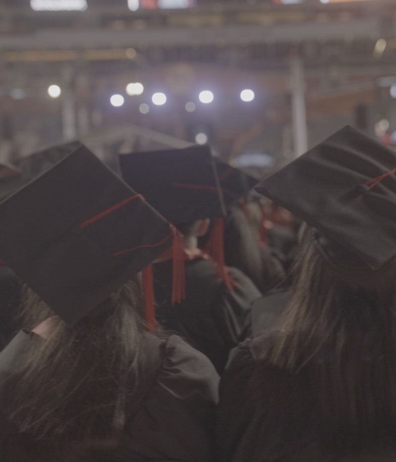 student in cap and gown raising thier hand making the longhorn symbol.